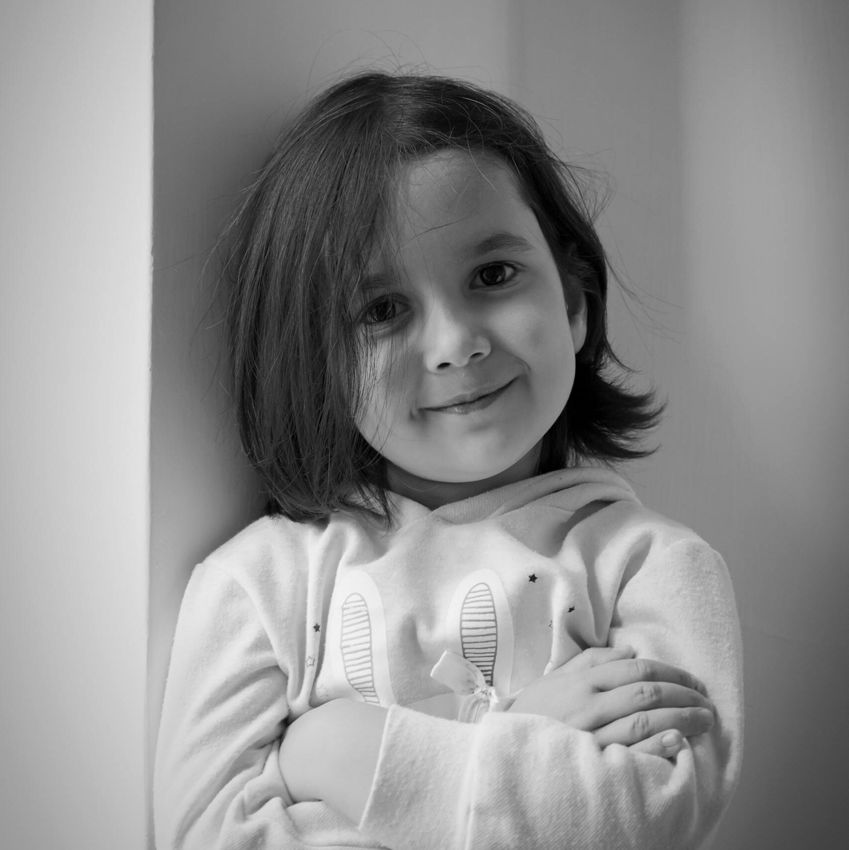 Black and white portrait of a smiling child in a hoodie, arms crossed.