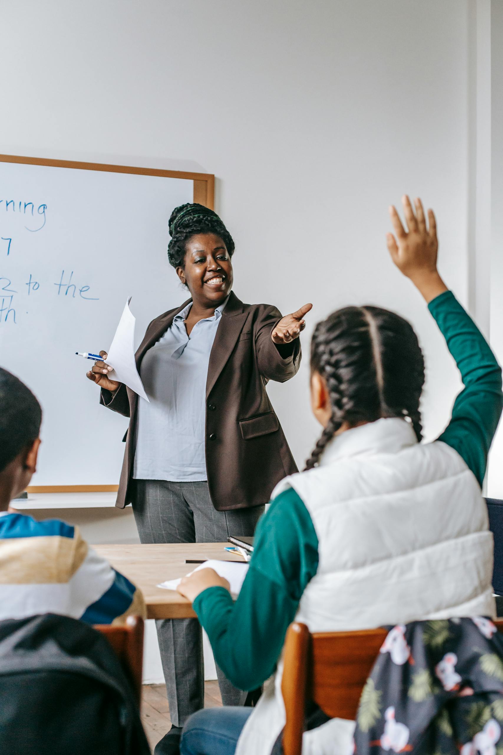 Smiling African American woman offering schoolgirl to ask question during lesson in school classroom